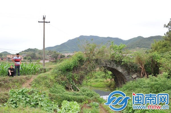 已廢棄的石拱橋，被野草覆蓋，下有溪流，村民稱此路